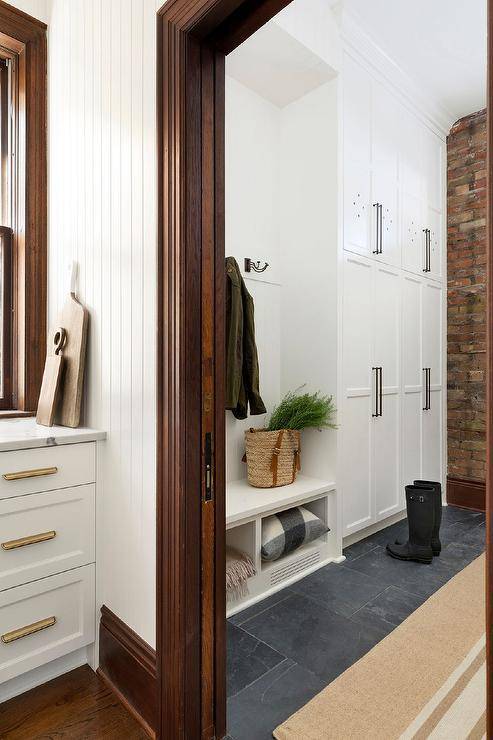 Cottage home with a galley style entry featuring floor to ceiling stacked cabinets and a built-in bench with cubbies. Slate floor tiles invite a dark finish contrasted with a warm French burlap runner.