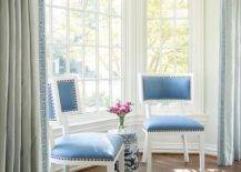 Blue velvet dining chairs sit in a bay window nook flanked by blue Greek key curtains.