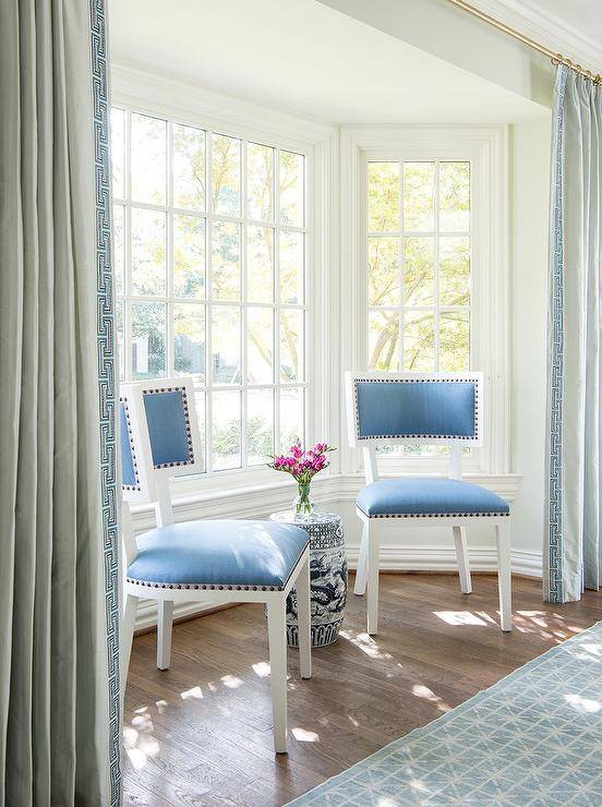 Blue velvet dining chairs sit in a bay window nook flanked by blue Greek key curtains.