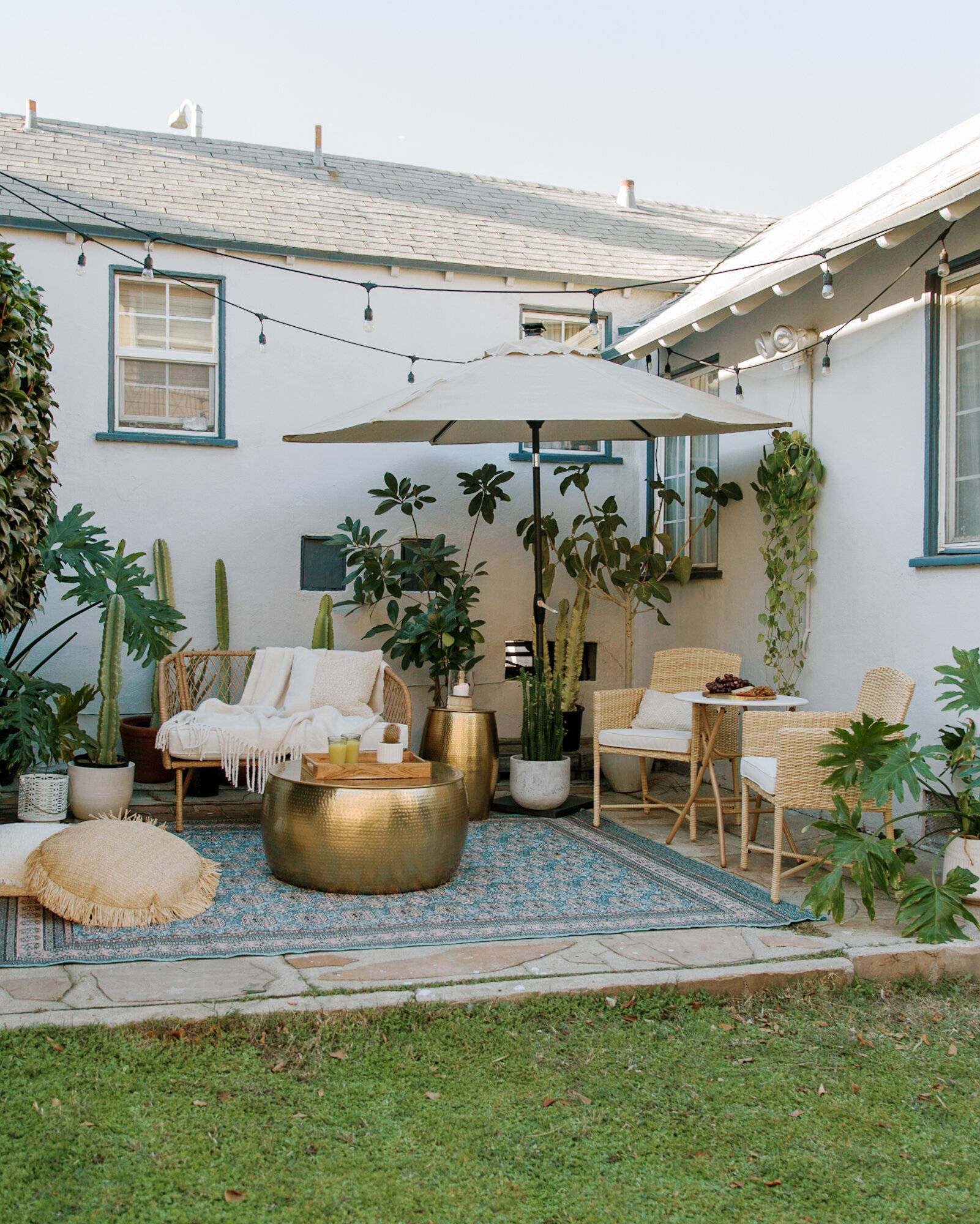 outdoor patio with open patio umbrella, string lights, gold dining room table and wooden furnture