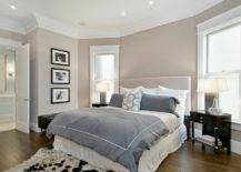Super master bedroom with greige walls paint color, light gray headboard, blue purple duvet & shams, white ruffled bedskirt, black & white cowhide rug, espresso stained glossy nightstands and crown molding.