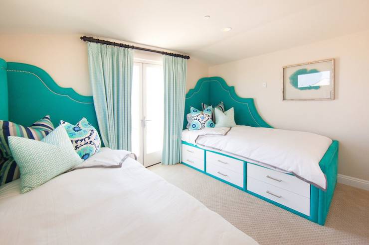 Amazing shared bedroom features daybeds with teal velvet corner headboards accented with silver nailhead trim while 6-drawers built into the two-tone daybed creates extra storage. White and teal daybeds are dressed in white and gray bedding as well as teal and purple suzani pillows, teal fretwork pillow and teal striped pillows flanking glass doors dressed in aqua curtains.