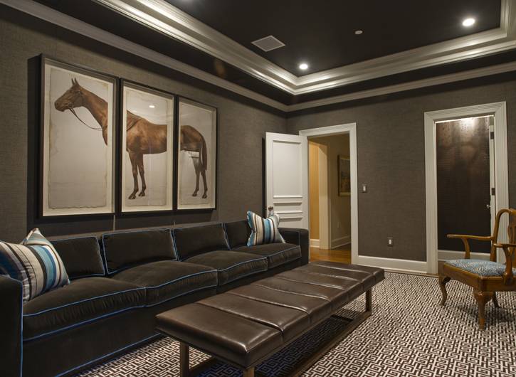 Amazing basement family room with taupe grasscloth wallpaper, white and brown Greek key rug, brown leather ottoman, chocolate brown velvet sofa with teal piping, horse triptych art, blue and brown striped pillows and tray ceiling painted dark brown.