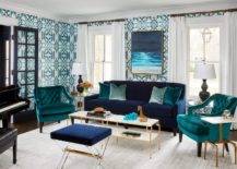 Jewel-toned room colors transform an ordinary room into a lovely eye-catching dwelling space. A long white and brass coffee table is centered atop alight gray rug between two teal velvet tufted accent chairs, a blue lucite stools and a blue velvet sofa with teal accent pillows. Blue and aqua wallpaper dress the walls neutralized by white window curtains and a black glass door panel.