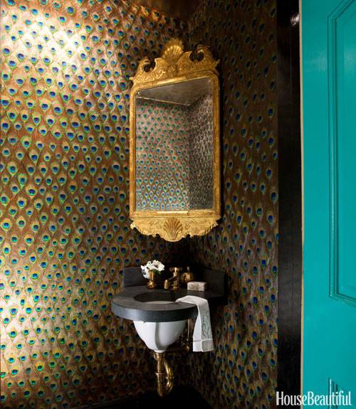 Turquoise door opens up to stunning tiny powder room featuring custom peacock feather wallpaper framing corner mirror, Georgian gold leaf mirror, over round corner sink.