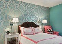 Gorgeous girl's room features accent wall clad in teal damask wallpaper and the rest of the walls painted teal. Chocolate brown tufted velvet headboard on queen bed is dressed in white and pink, monogrammed bedding flanked by polished nickel, swing-arm sconces over single nightstand, white studded nightstand, to the left and pink chevron chair to the right.