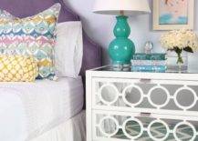 Pretty girl's room with arched purple headboard layered with white bed linens topped with pastel colored pillows situated next to a Worlds Away Ava Nightstand topped with a teal double gourd lamp with framed kid's art above over hardwood floors layered with a teal chevron rug, Jill Rosenwald by Surya Fallon Arrows Teal Hand Woven Flatweave Rug.