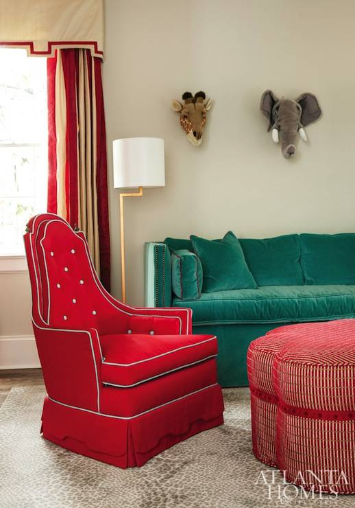 Amazing kids' room features toy elephant head and toy giraffe head over high-back teal velvet sofa next to antique brass floor lamp. Chic kids' room with tan fretwork valance with tan and red striped curtains paired with red velvet tufted chair and red clover ottoman over leopard print rug.