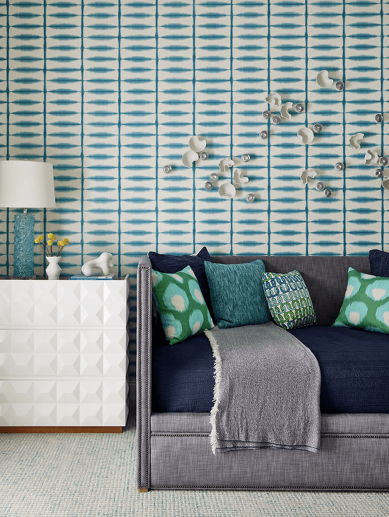 Gray and blue boy's room features a dark gray daybed with green Ikat pillows and a dark gray throw, blue and green bedding, white and blue wallpaper and a white bedside table lit by a blue lamp.