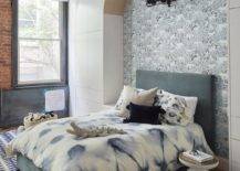 Dark gray bed in an arched niche decorated with blue and white wallpaper finished with a bronze sconce in a contemporary bedroom. A white and blue rug adds a mismatched pattern to the loft room creating appeal in all corners.