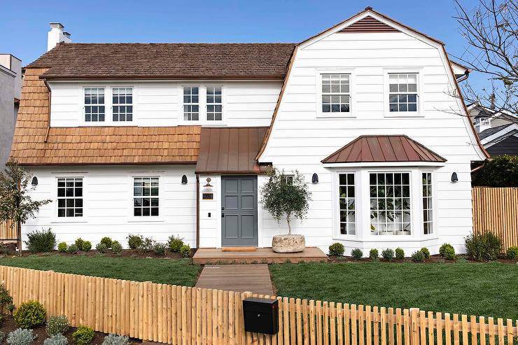 A charcoal gray front door accents a white lap cottage home finished with a gorgeous shingles roof.