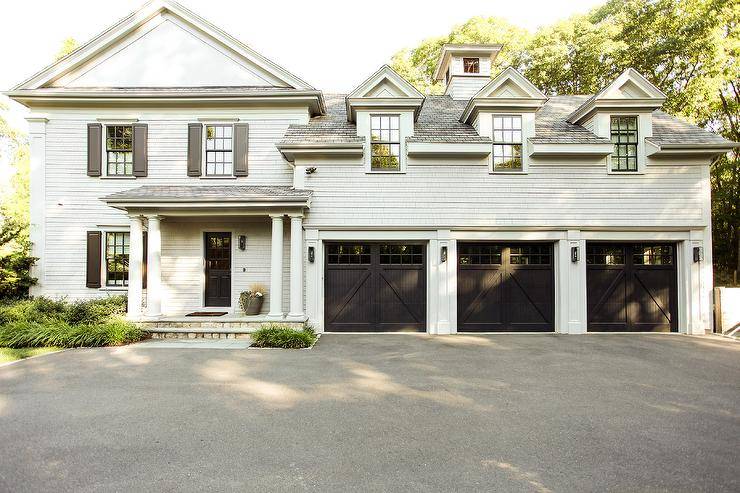 Light gray shake siding home boasting a black front door, two-car garage, and gray shutters with doric columns. The covered porch and greek columns invite a stunning curb appeal to the home property.