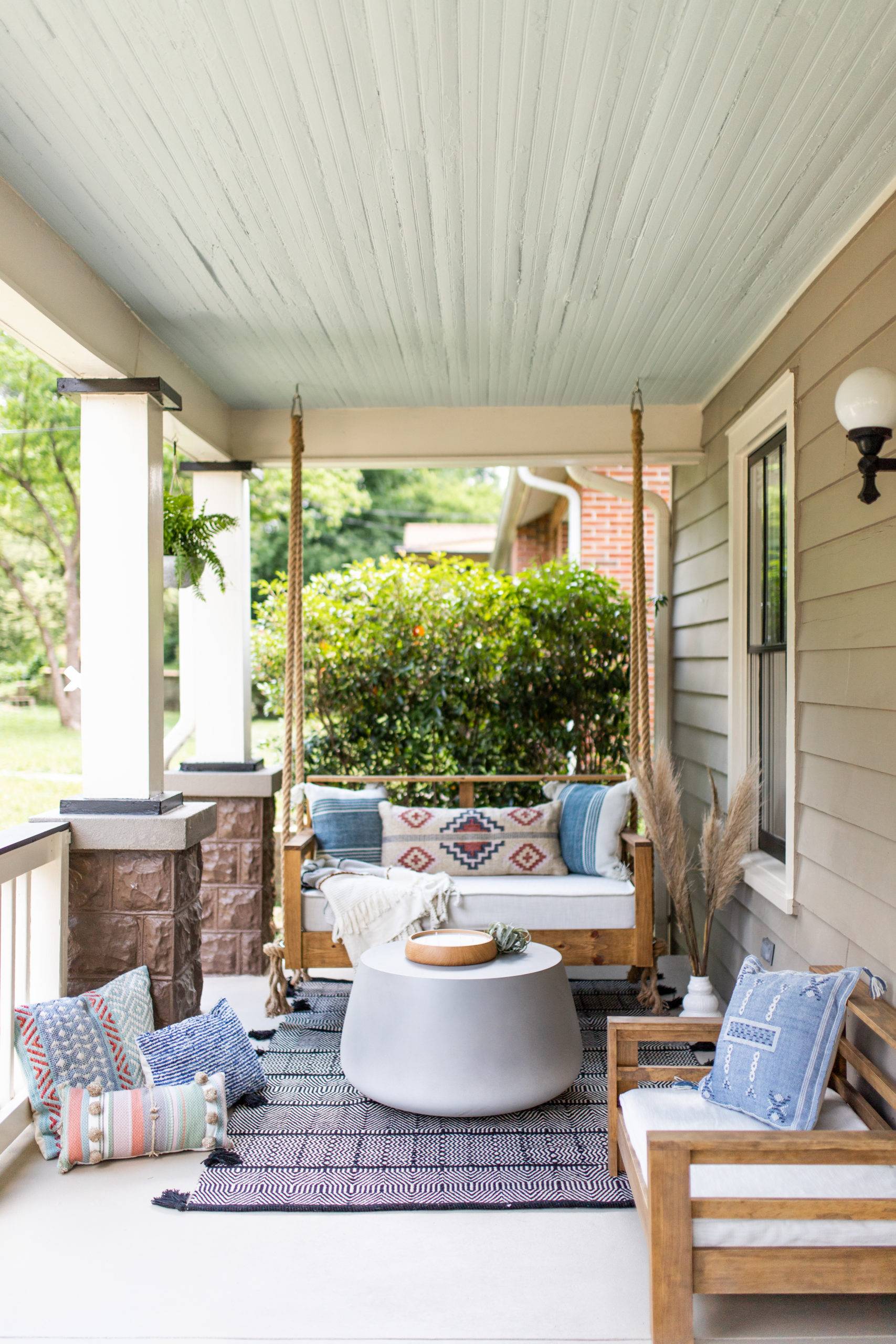 boho styled front porch with wooden swing, bohemian rugs and pillows, white center table
