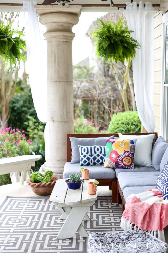 outdoor patio with geometric rug, grey outdoor sofa and colorful floral pillows