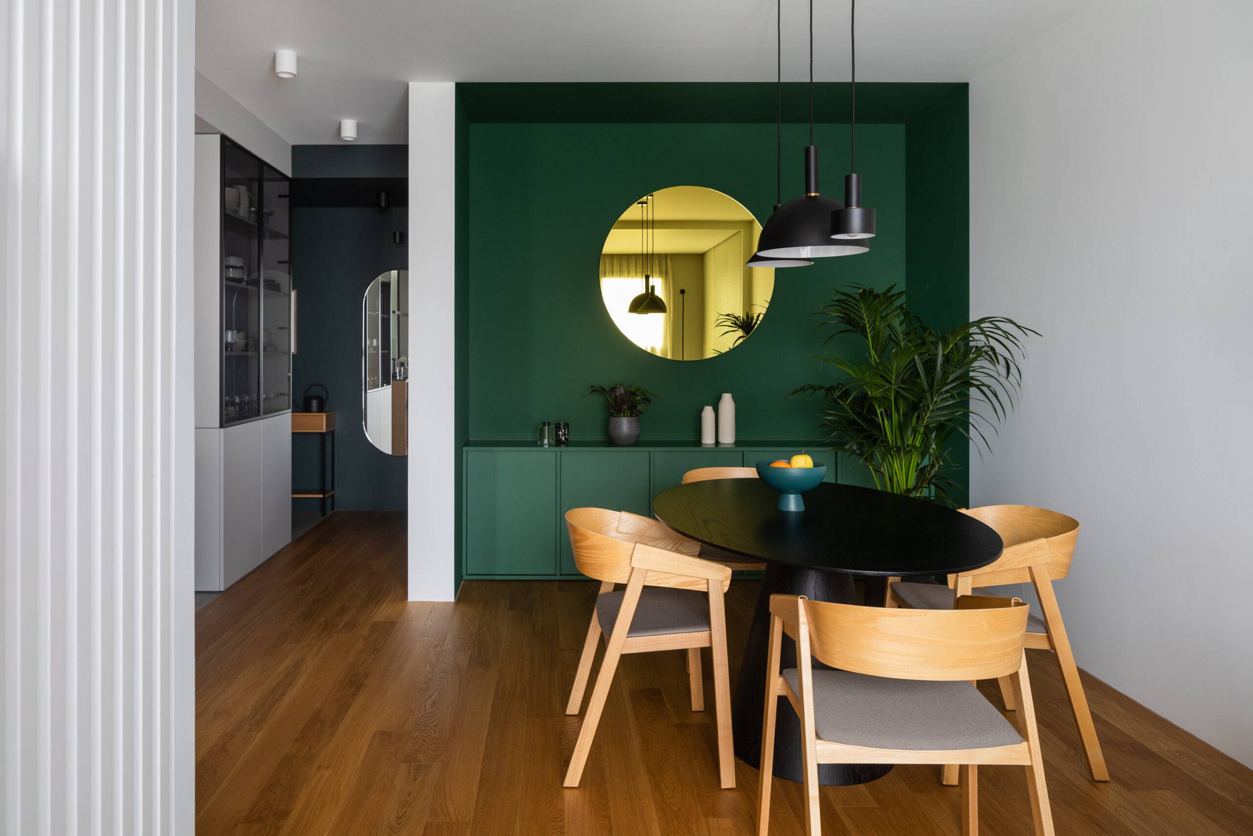 round mirror mounted on dark green wall in dining room with wooden furniture