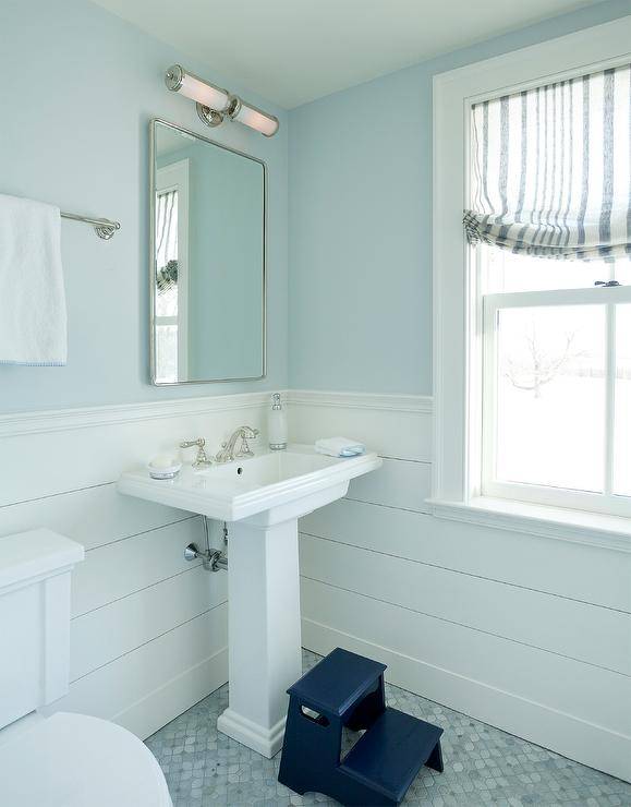 White and blue boys' bathroom features blue walls lined with white shiplap trim and holding a curved nickel mirror over a white pedestal sink with a polished nickel faucet kit. The washstand is fixed to gray mosaic marble floor tiles.