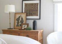 A gold bamboo lamp complements a farmhouse dresser styled with layered art and placed under a framed fabric art piece.