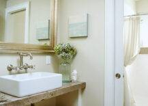 Lovely coastal bathroom design with cafe au lait walls paint color, silver leaf beveled bathroom mirror, brushed nickel bridge wall-mount bathroom faucet, reclaimed wood bathroom vanity shelf, pocket doors and white overmount sink.