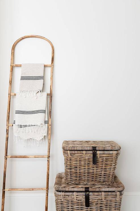 Cottage bathroom features a vintage towel ladder placed beside stacked wicker trucks.