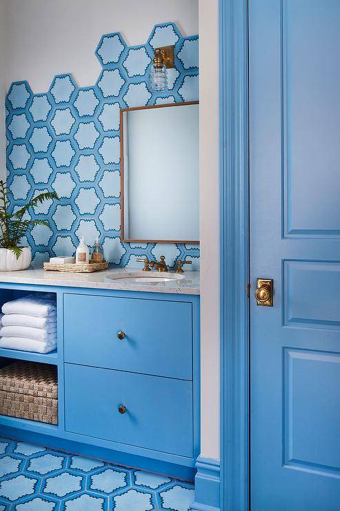 Blue cottage bathroom featuring a blue washstand with a gray quartz countertop and blue hexagon backsplash tiles. Brass hexagon knobs deliver a warm finish contrasting the cool hues with a elegant touch.