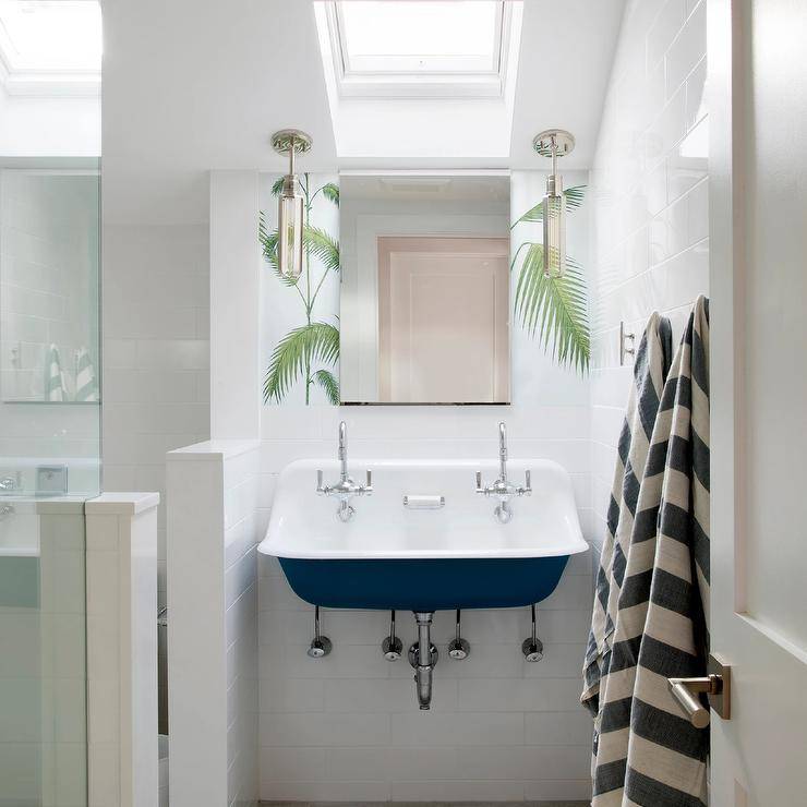 Kids cottage style bathroom features a navy blue trough sink with dual vintage faucets on large white subway tiles and a skylight.