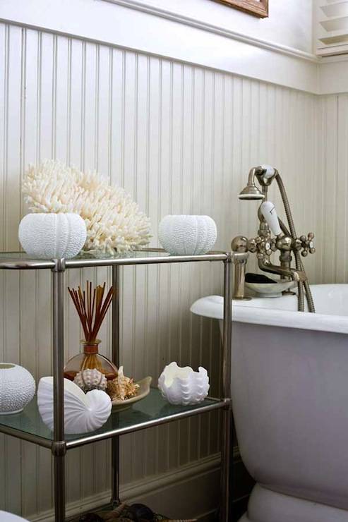 Beachy bathroom with white beadboard walls, nickel glass-top bathroom etagere, white seashells, beachy accents, freestanding tub and brushed nickel vintage tub filler.