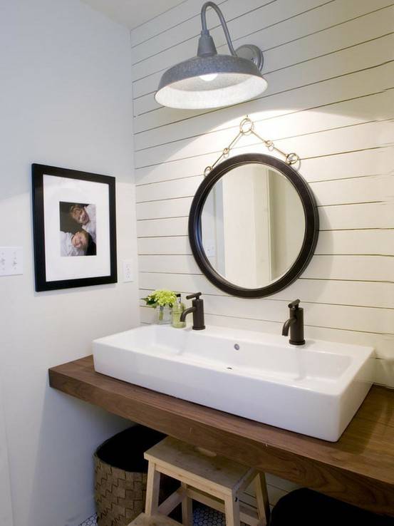 Coastal powder room design with paneled accent wall, chunky wood floating bathroom vanity, rectangular white porcelain sink, woven baskets and black convex mirror.
