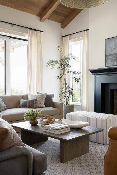 Living room features gray cube ottomans in front of a black fireplace mantle, wicker chain rings on coffee table books atop an oak coffee table and a gray sofa.