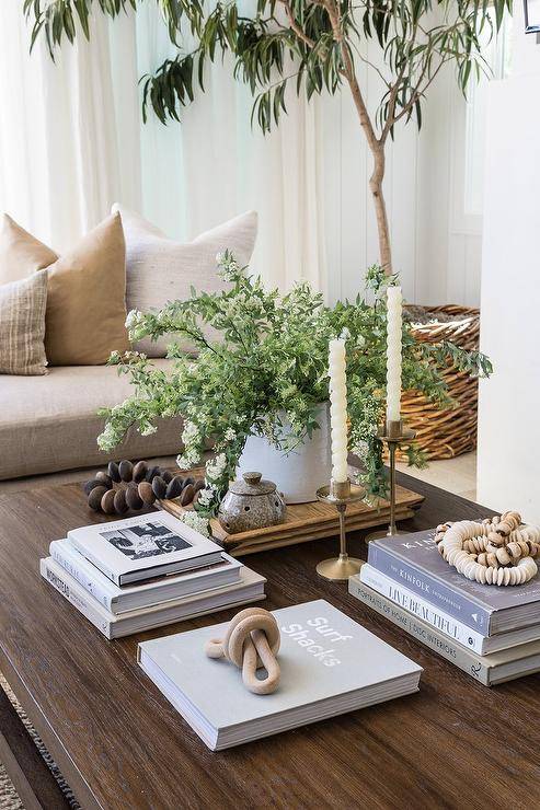 A dark brown styled coffee table is accented with stacked coffee table books and vintage brass candle holders.