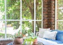 Red brick sunroom features a black daybed and a Moroccan style round hammered metal coffee table on a fringe jute rug.