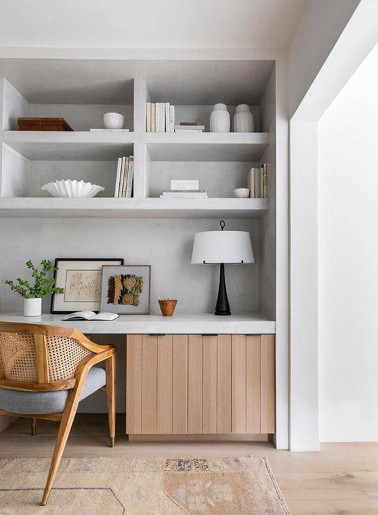 A vintage cane chair sits at a concrete top desk with slatted cabinets and concete shelves.