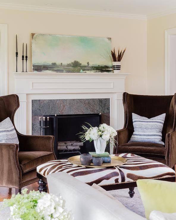 Transitional living room featuring chocolate brown velvet wingback chairs in front of a fireplace facing a zebra bench as a coffee table.