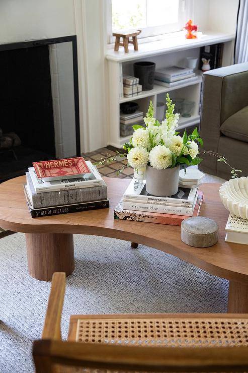 On a light gray rug, a vintage kidney shaped coffee table is accented with stacked coffee table books and positioned in front of a dark gray sofa.