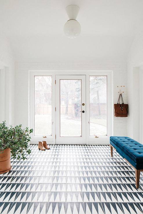 Cool and Eclectic foyer features a blue velvet tufted storage bench placed on a black and white geometric tiled floor.
