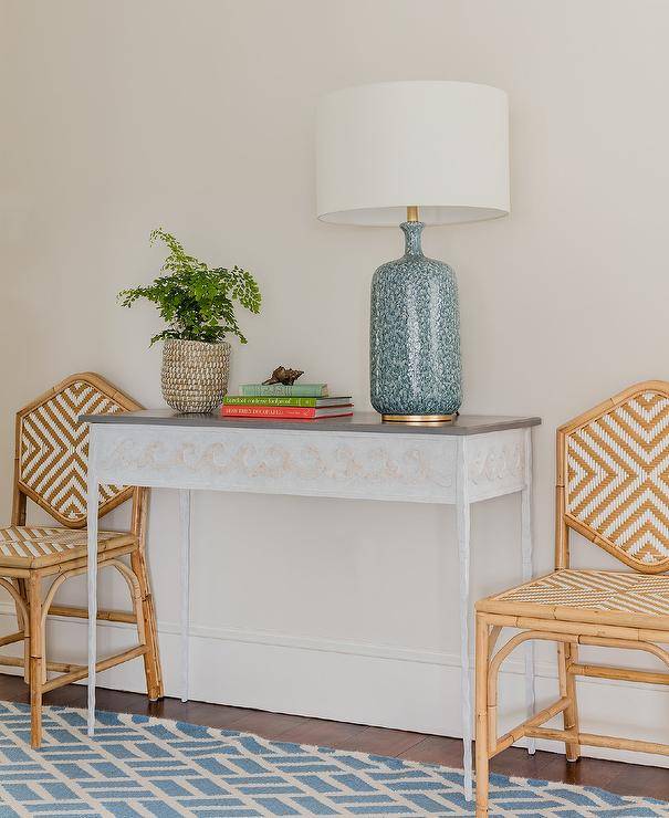 Rattan chevron chairs sit on a blue geometric rug and flank a white and gray console table topped with an Aerin Culloden Lamp.