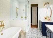 This master is very elegant with it’s navy vanities, marble tile and of course brushed gold fixtures. The blue lacquer vanities add a coastal feel while providing contrast with white quartz countertops, shiplap bathroom walls and white herringbone shower tiles. The claw foot bathtub features a polished brass vintage tub filler that surely compliments the gold accents in the room such as the round gold frame mirrors and and brass vanity sconces. Gray and white marble basketweave floor tiles also add personality and dimension in this gorgeous contemporary bathroom.