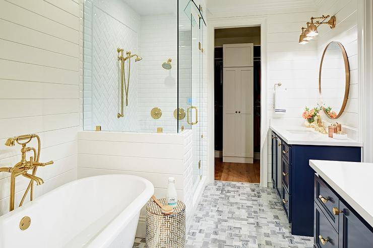 This master is very elegant with it’s navy vanities, marble tile and of course brushed gold fixtures. The blue lacquer vanities add a coastal feel while providing contrast with white quartz countertops, shiplap bathroom walls and white herringbone shower tiles. The claw foot bathtub features a polished brass vintage tub filler that surely compliments the gold accents in the room such as the round gold frame mirrors and and brass vanity sconces. Gray and white marble basketweave floor tiles also add personality and dimension in this gorgeous contemporary bathroom.