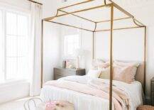 Chic girl's bedroom features a gold canopy bed with white and pink bedding flanked by gold and gray nightstands, white tolix mini chairs with a pedestal accent table at the foot of the bed, a pink pouf and a pink and gray rug.