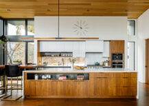 A mid-century modern kitchen with white cabinets, built-in storage within the island, and dark wood accents.