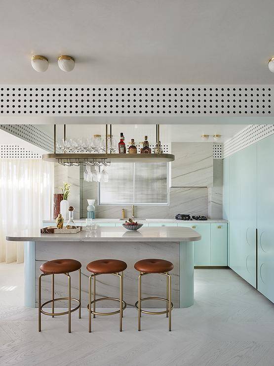 Kitchen features a modern light blue island under a brass bar shelf, brown leather swivel stools and light blue cabinetry with brass trim.