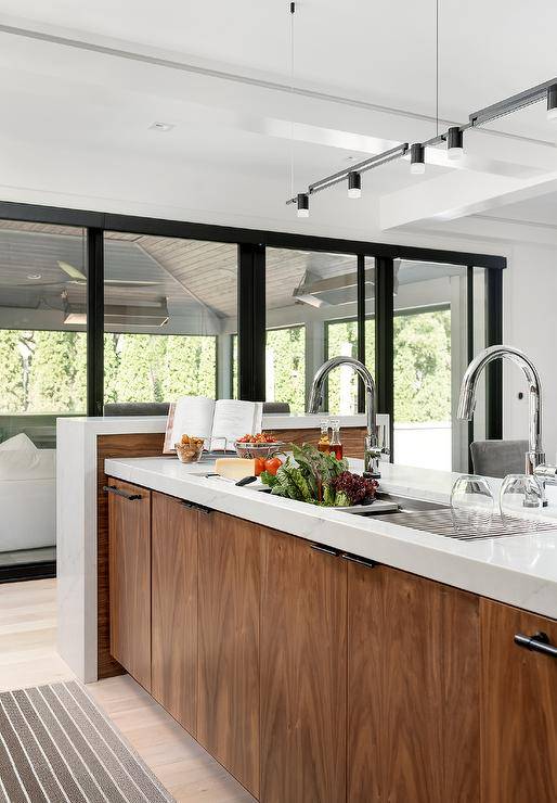 A brown veneer kitchen island is fitted with a wide stainless steel sink paired with two chrome gooseneck faucets