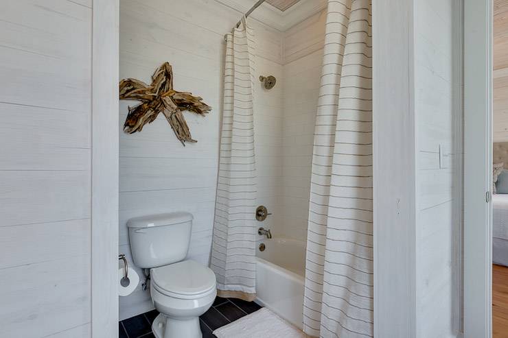 Coastal bathroom features whitewashed oak paneled walls framing driftwood star over toilet next to drop-in tub accented with subway tile shower surround dressed in striped double shower curtains.