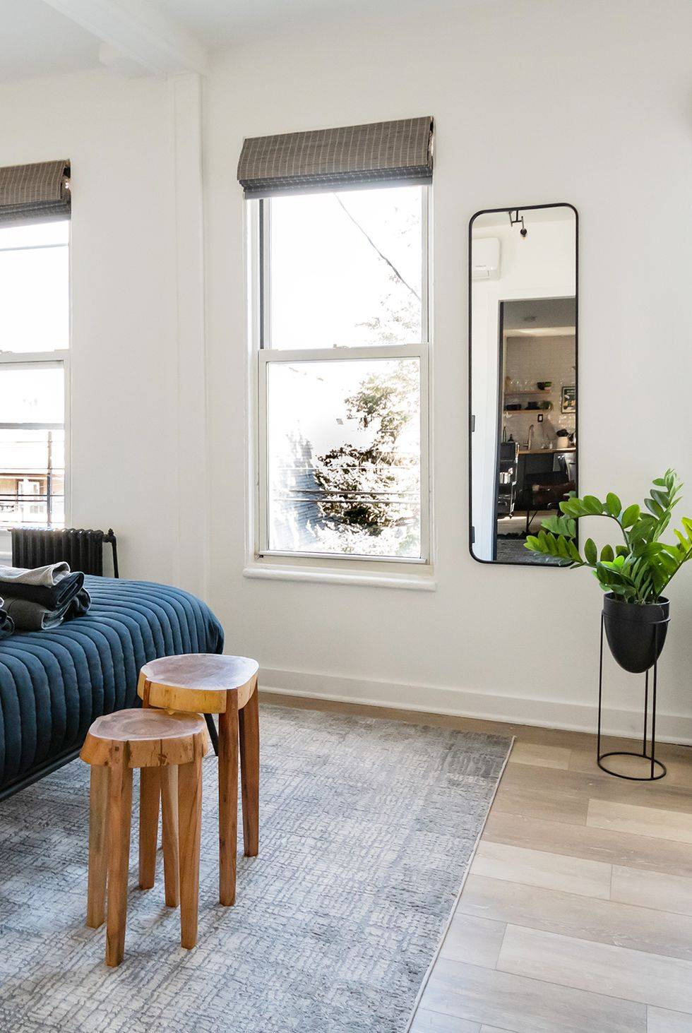 open studio apartment with rug two wooden stools white walls black frame mirror