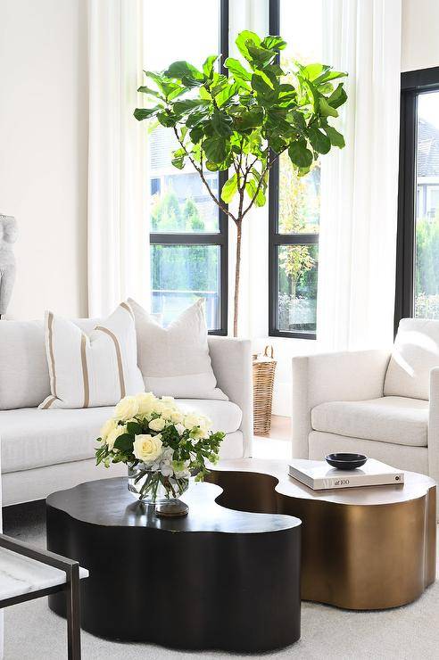 white living room boasts gold and black puzzle piece-shaped coffee tables and a white sectional with florals and gold accent