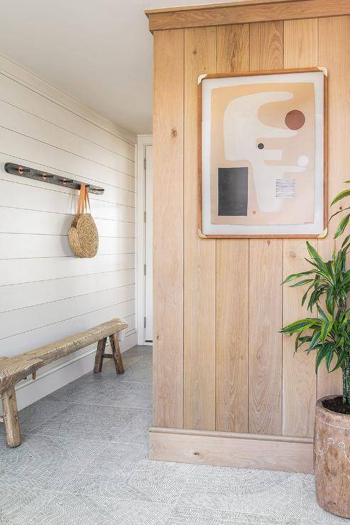 A black row of hooks is mounted in a foyer against a white shiplap wall and over a long reclaimed wood sawhorse bench.