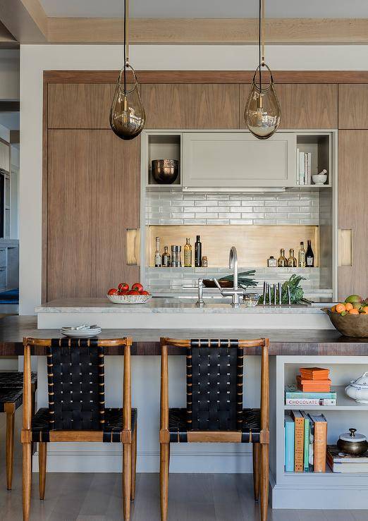 Wonderfully designed modern kitchen boasts wood and black woven leather stools placed at a wood top island finished with cookbook shelves.