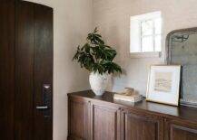 An arched brown wooden door opens to mosaic floor tiles accenting a foyer boasting a built-in credenza placed under a window and topped with a silver leaf beaded mirror.