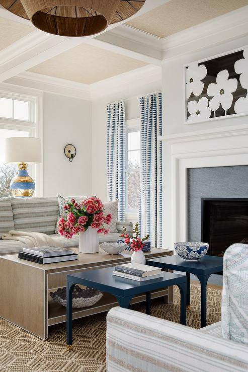 Brown and blue striped sofas sit face to face flanking side-by-side blue accent tables and a tan tiered coffee table.