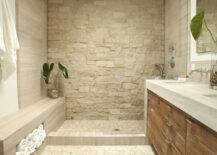 Zen bathroom features open shower clad in stone surround as well as stone shower bench accented with cubby filled with fluffy white towels across from reclaimed wood double vanity topped with stone countertop paired with wall-mounted faucets atop pebble floor.