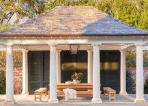 Gorgeous white pool house boasts Greek columns and is contrasted with black shutters doors.